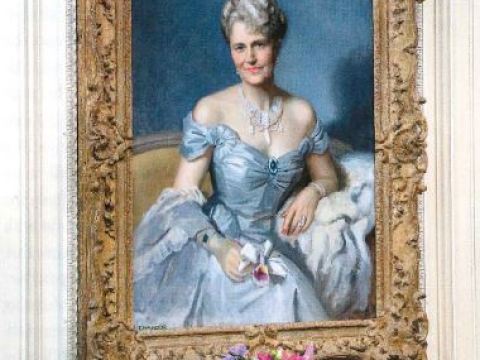 A portrait of a grey haired woman in a white dress hangs above an ornate fireplace.