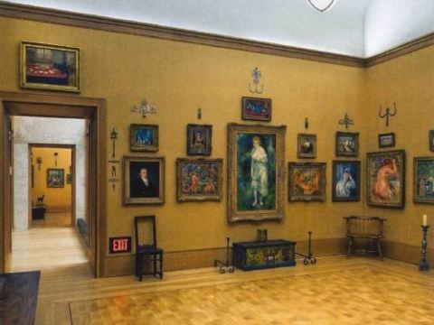 Multiple paintings and portraits hang in a light brown room.