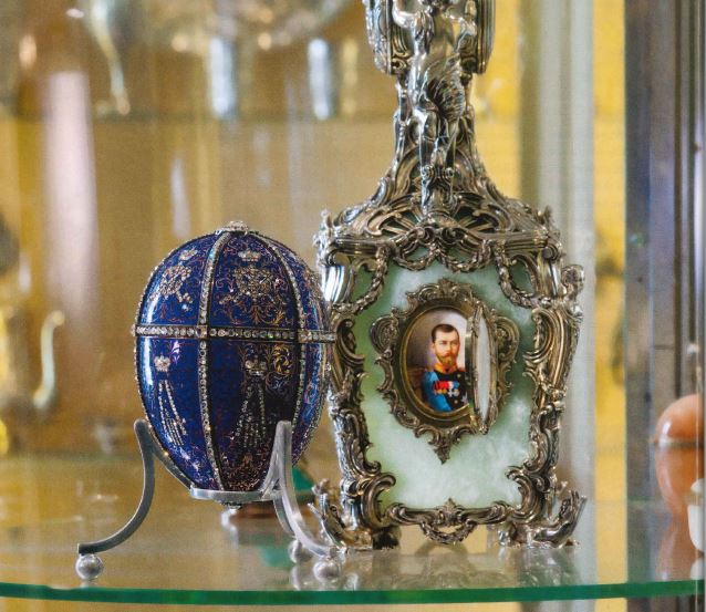 Ornate decorations, such as a bejeweled blue egg and a depiction of a Russian monarch, sit on a glass table
