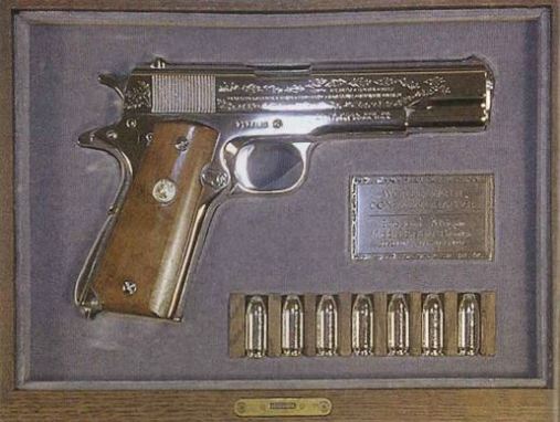 Image of a handgun on display in a velvet lined box with six bullets also on display.