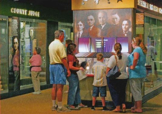 A group of people surround an exhibit panel. 