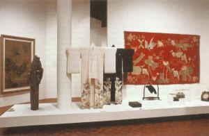 Two kimonos on stands with various other artifacts on a plinth in a gallery. 