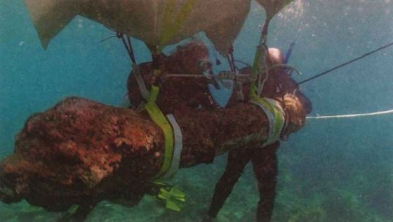 Two divers hold onto an encrusted object tied with line to a floating piece pulling it from the depths.