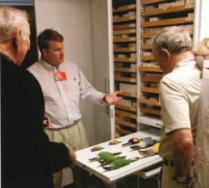 Three men stand looking at a pulled out storage drawer.
