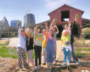A group of children holding up carrots that they picked in the Greensboro Children's Museums' edible schoolyard.