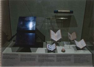 View of the interior of a case with a wooden object and several open books on display. 