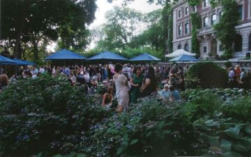 View of an outdoor event with a large group of people milling about under canopies in a garden.