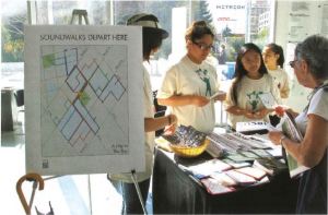 Young students stand behind a table with various brochures on it talking to a woman interested in the program. 