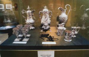 Display case with a pair of slave shackles and silver vessels in Metalwork 1793-1880.