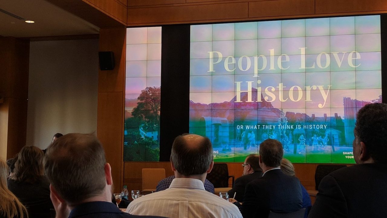 View of the conference room where the historic house summit was held with a group of mainly men looking at a screen with "People Love History" displayed on it.