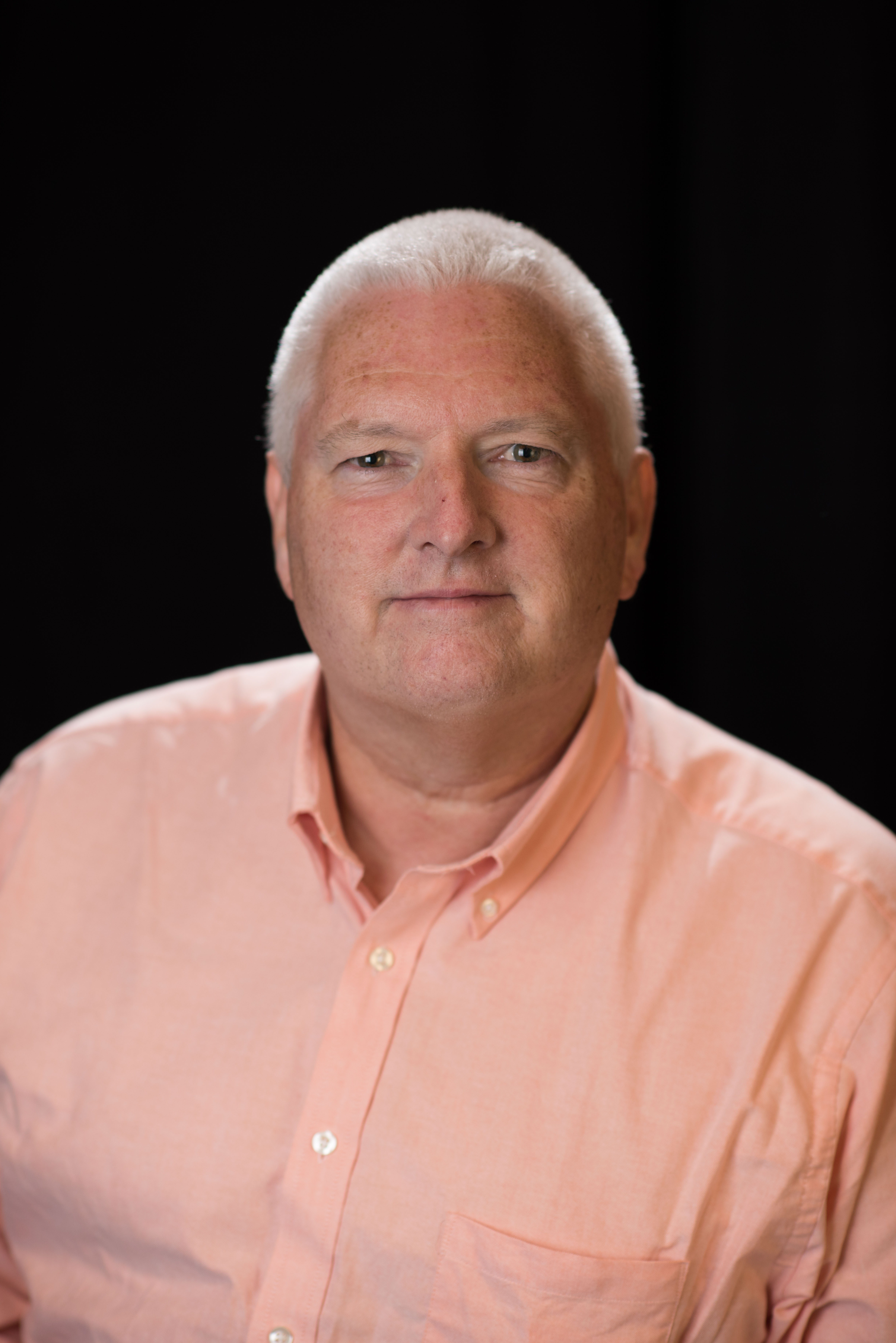 Headshot of a man with grey hair wearing a peach colored shirt.