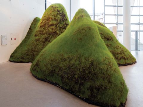 Four mounds of grass sit directly on the floor in an interior exhibition space. 