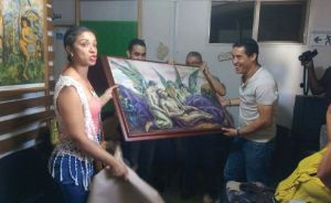 A Hispanic woman and three Hispanic men hold up a piece of framed art with angels in it. 