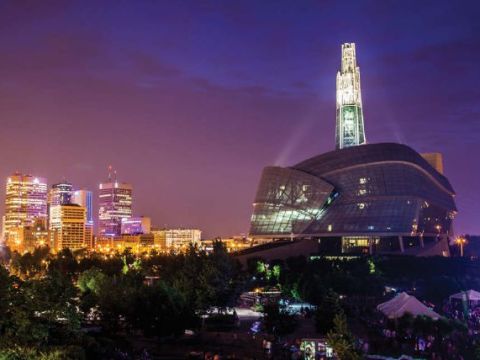 Night skyline with a towering highrise with lights shining on it and the museum in the foreground also with lights.