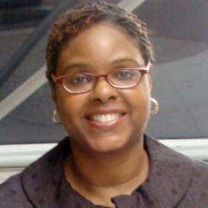 Headshot of a black woman with short red highlighted hair wearing red horn rimmed glasses smiling straight at the camera.