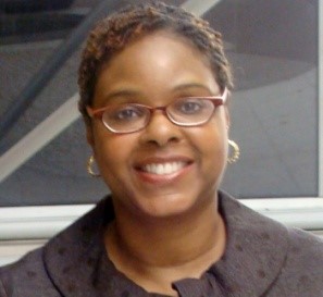 Headshot of a black woman with short red highlighted hair wearing red horn rimmed glasses smiling straight at the camera.