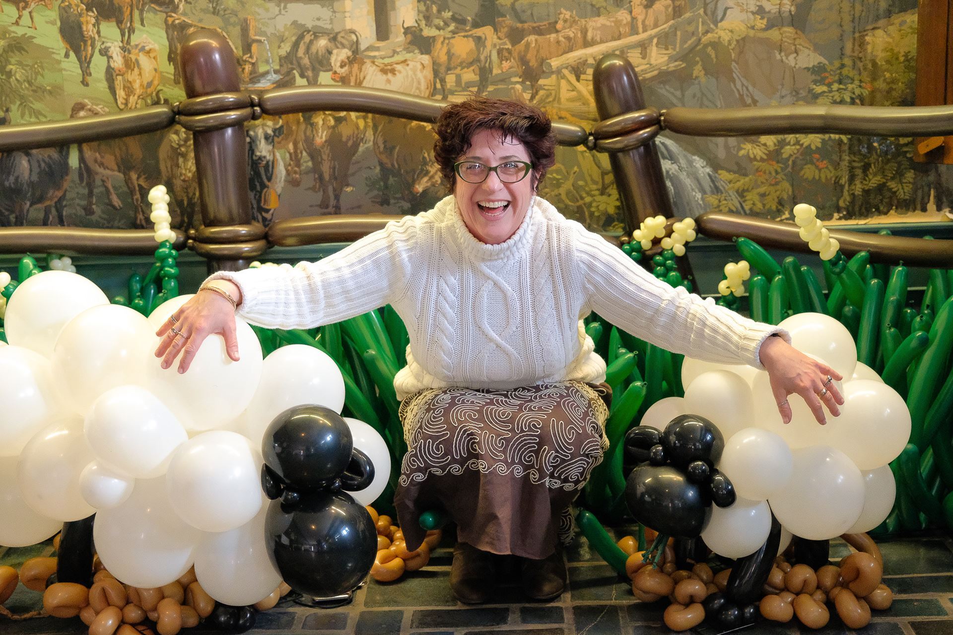 A woman crouches down next to two glass sheep in a fake paddock.
