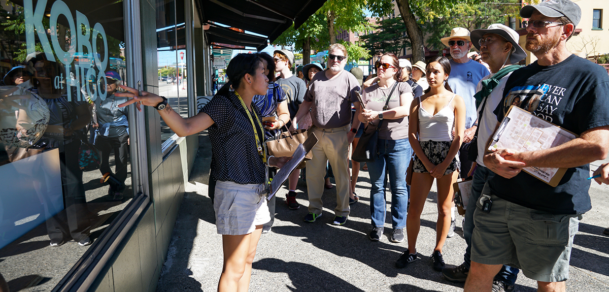 A tour guide discusses one business at a storefront with a diverse group of individuals.