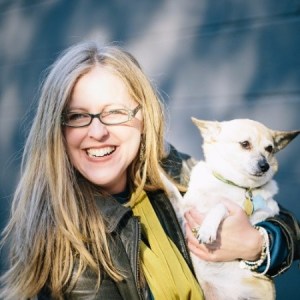 Headshot of Jen Phillips April with a corgi dog under her left arm.