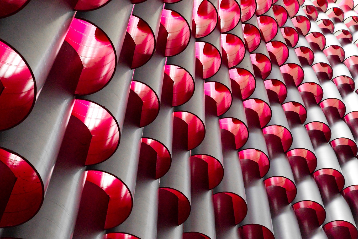 Round tubes stacked on top of each other with bright pink interiors creating a glowing tower.