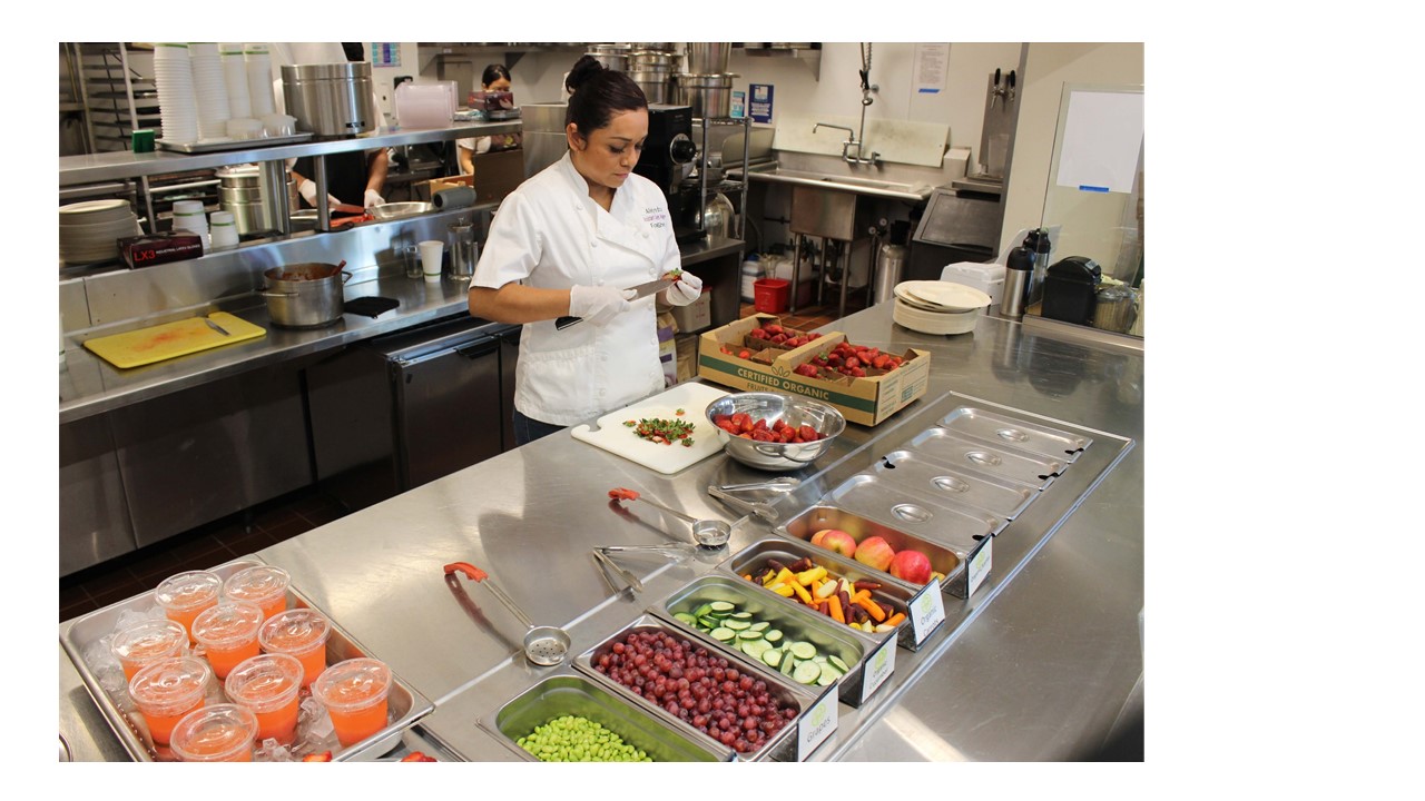 View of the FoodShed kitchen with an Hispanic female chef cutting fruits and vegetables.