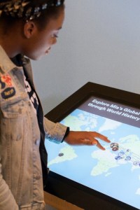 A young black woman using her fingers to manipulate the interactive map on a kiosk screen. 