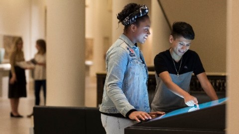 A young black girl and a brown boy look down at an interactive kiosk in the museum.