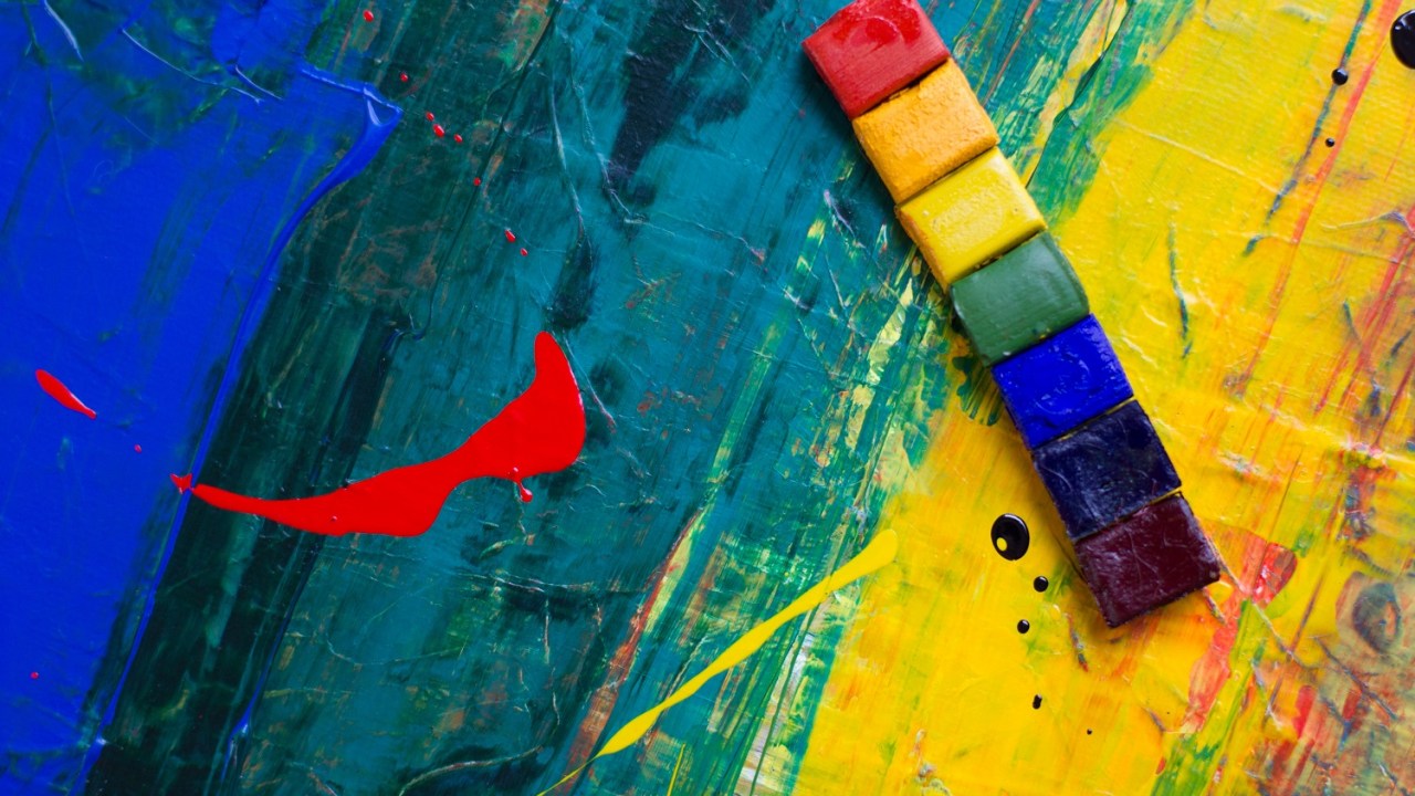 Closeup of a canvas with stron g green red yellow and blue paint and a strip of rainbow colored paint squares to the right of the image.