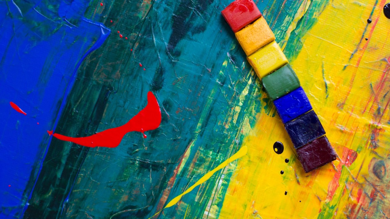 Closeup of a canvas with stron g green red yellow and blue paint and a strip of rainbow colored paint squares to the right of the image.