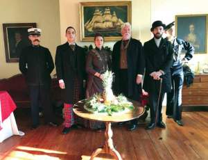 A group of five individual stand in the room of a historic house wearing period costume posing for the picture.