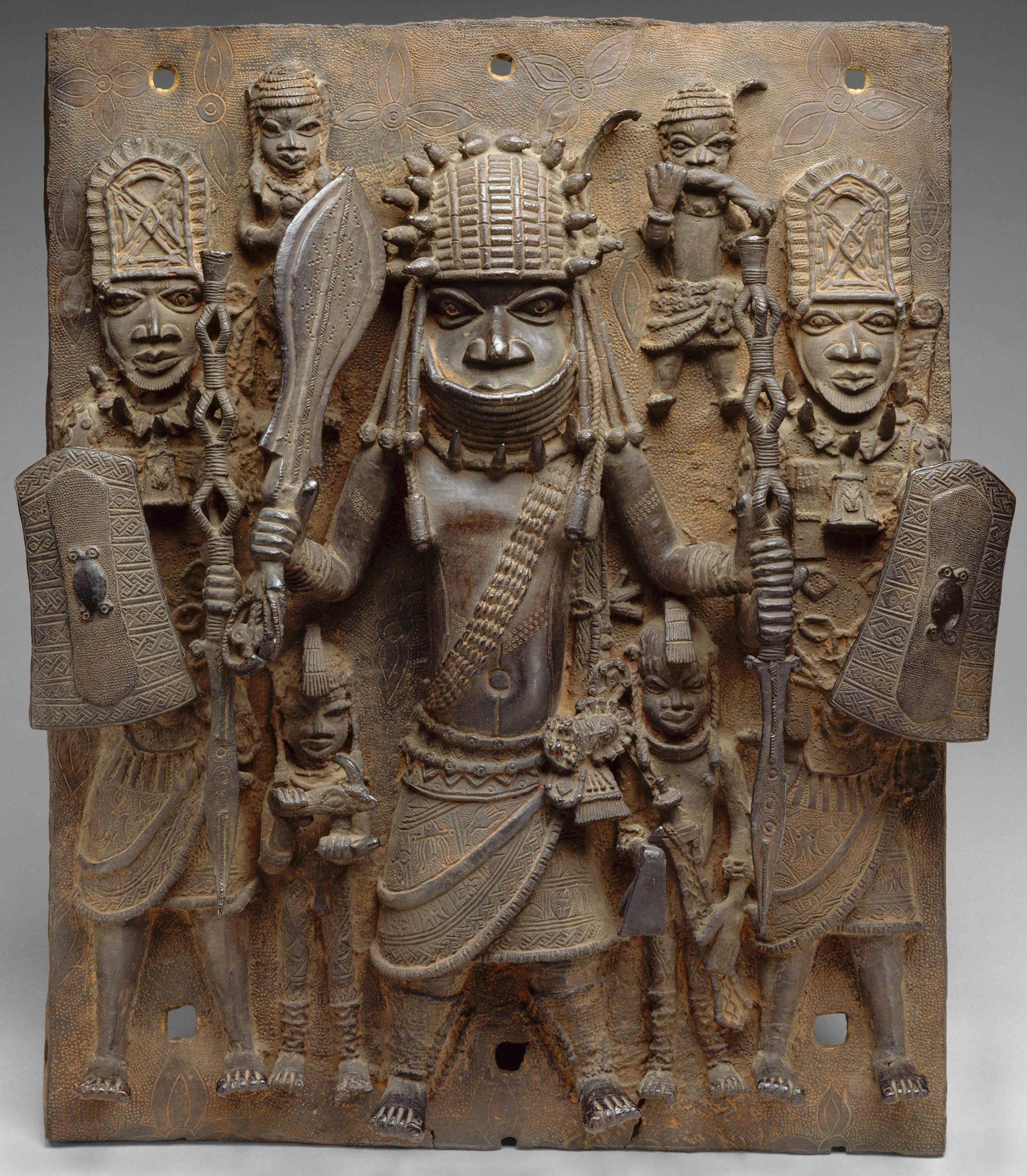 A plaque from Benin featuring what appear to be three soldiers in loincloths headdresses. They are brandishing clubs and shields.