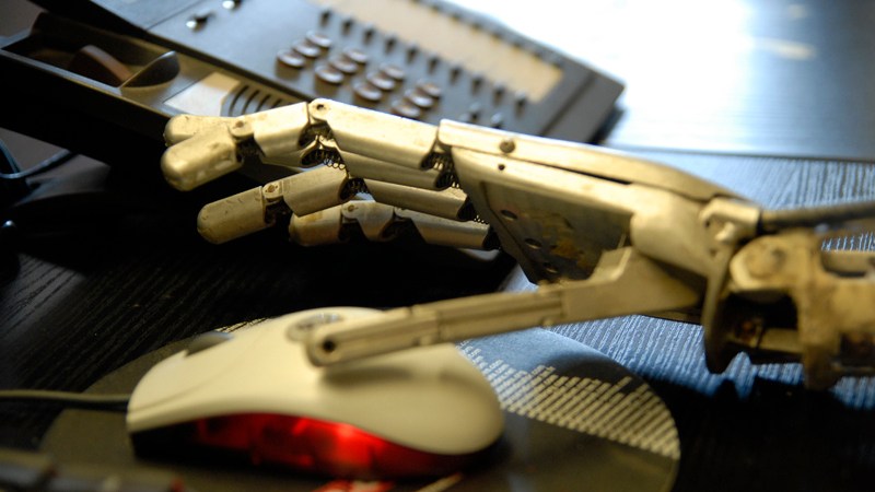 A robotic hand is shown reaching for a computer mouse, with a desktop phone in the background, in a vivid if not entirely accurate illustration of artificial intelligence coming to the museum workplace.