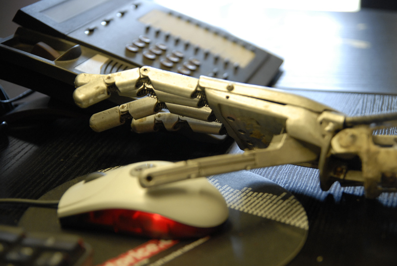 A robotic hand is shown reaching for a computer mouse, with a desktop phone in the background, in a vivid if not entirely accurate illustration of artificial intelligence coming to the museum workplace.