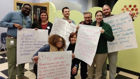 A group of six individuals holding up large white sheets of paper with various mission and vision statements written on them.