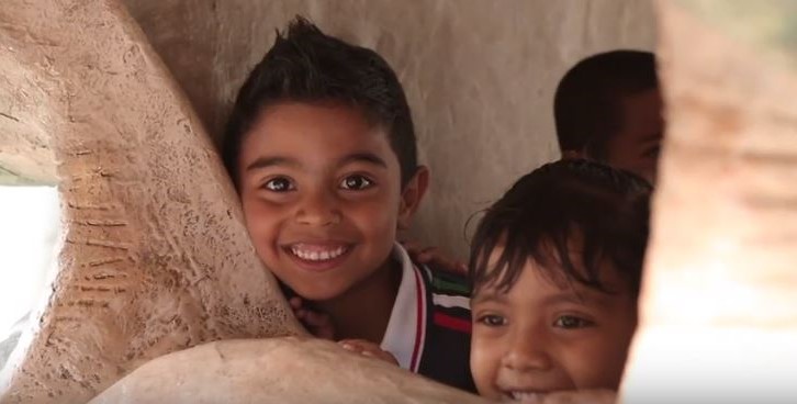 Two young children smile out from within a dinosaur sculpture.