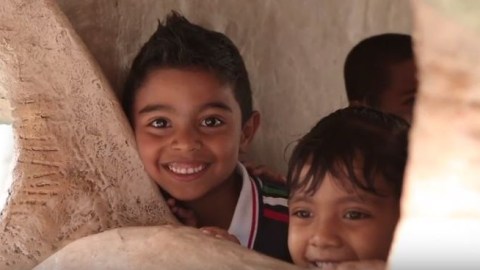 Two young children smile out from within a dinosaur sculpture.