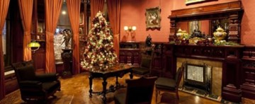 A photo of the interior of the Richard H. Driehaus Museum, the site of the panel discussion "How can I better support my LGBTQ co-workers," comprised of LGBTQ museum staff and part of CAMP's meeting schedule. The photo shows a sitting room with table and chairs, a fireplace, and a Christmas tree.