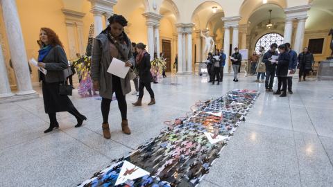 A young black woman stands in a museum inspecting a flat printed piece that is displayed on the floor.