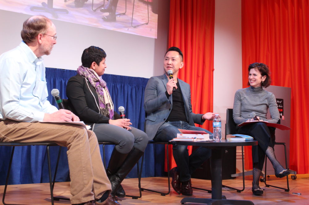 Four people sit around a table on stage holding microphones.