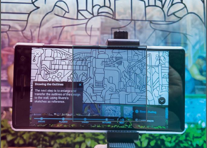 Image of a handheld device being held up in front of the fresco showing a description of the piece and applied color over portions to help explain what is happening.