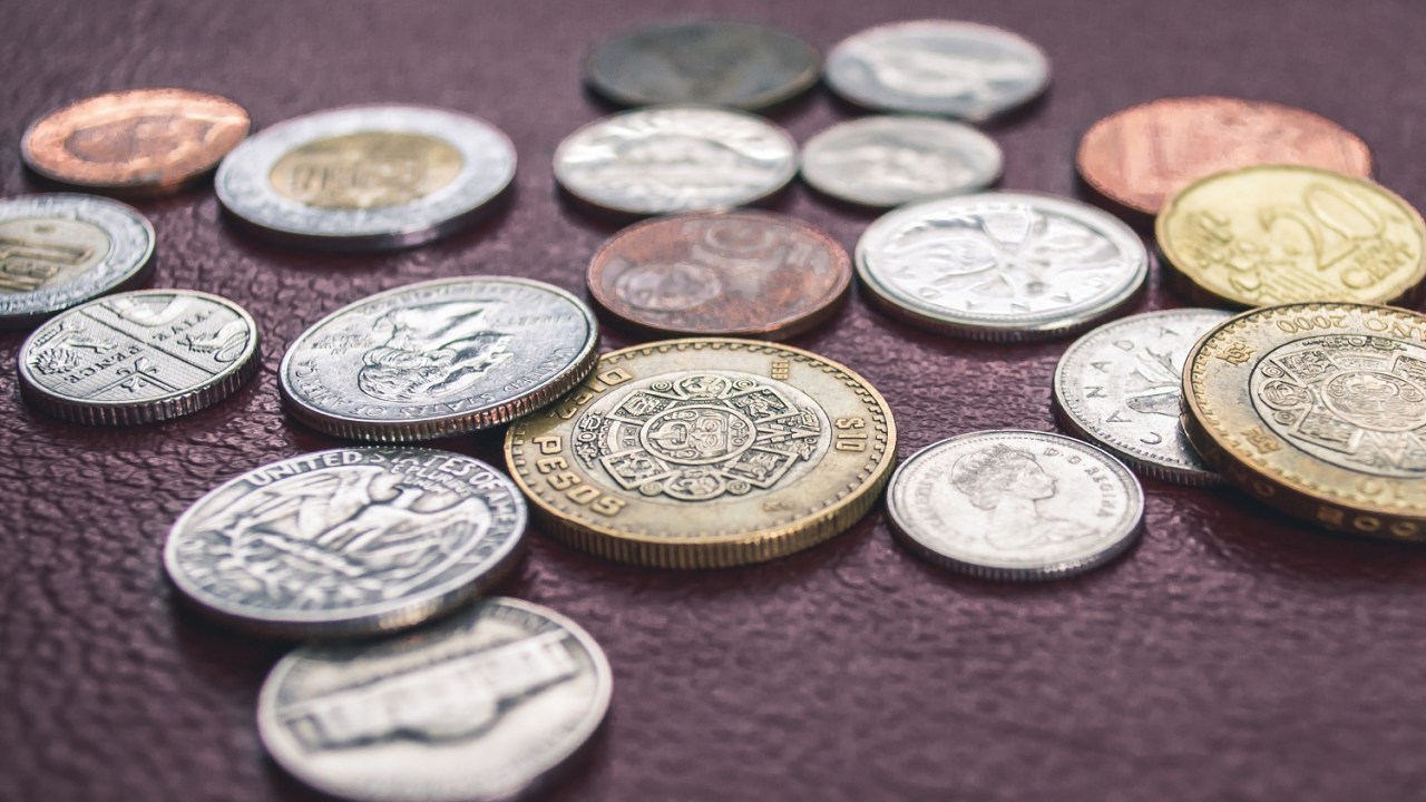 Image of a variety of coin money from around the world displayed next to and one on top of the other on a wooden background.