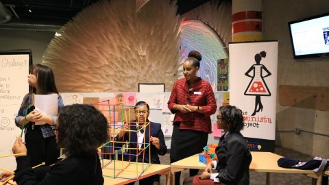 Dr. Tonya Matthews speaking in a museum classroom setting with several people sitting on chairs listening to her.