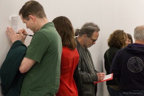 People stand huddled writing on pieces of paper.