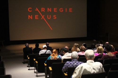An auditorium of people look at a screen with the logo for "Carnegie Nexus" on it.