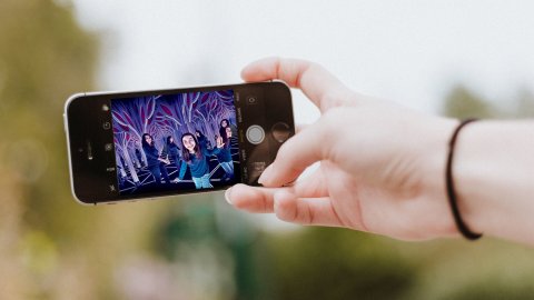 A person's hand holds a smartphone displaying a photograph of one child and one adult frolicking in a mirrored art installation that appears to stretch into infinity, an example of the sort of installations that attract outsize attendance and social media pickup.