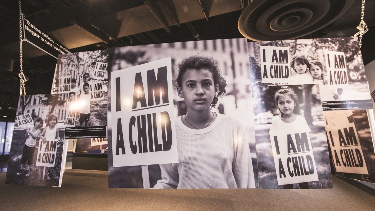 Interior shot of the I AM A CHILD exhibition with a large format photogrpah of a young Hispanic girl holding a sign that says "I AM A CHILD".