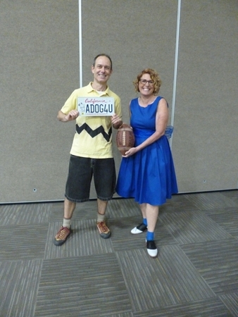 Phil Kohlmetz wears a handmade recreation of Charlie Brown's famous outfit: a yellow polo shirt with a zigzag across the waist, black shorts, and brown shoes. He holds one of the Snoopy license plates. Shawn Lum recreates Lucy's standard outfit with a blue dress and black-and-white saddle shoes, and holds a football, a reference to a famous Peanuts tableau.