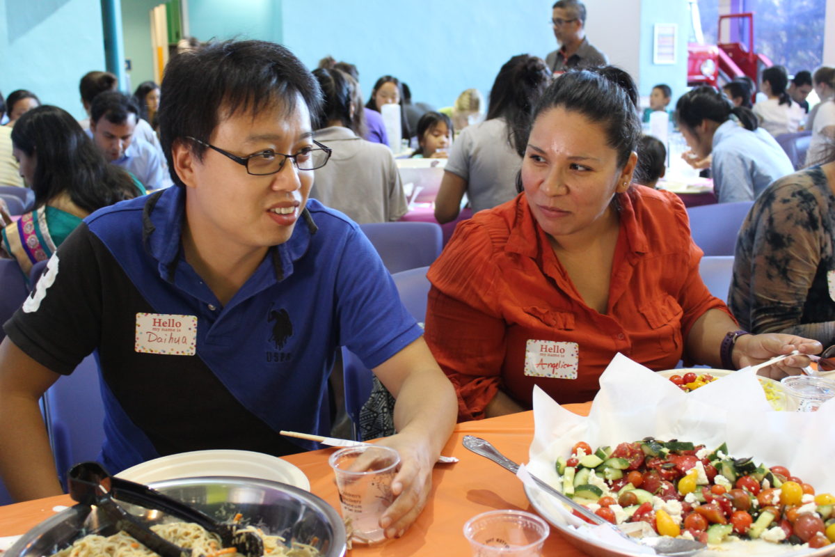 An Asian man sits next to a Latina woman at a meal, engaged in conversation.