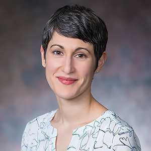 Headshot of Carla Galfano, a white woman with short dark colored hair wearing a patterned white with black top.