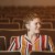 Image of Hannah Hethmon sitting in a theater alone turning her head to the side wearing a striped top.